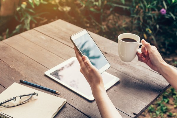 Nahaufnahme einer Person, die ein Handy und eine Tasse Kaffee in der Hand hält.