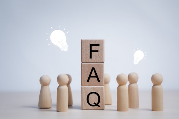 Drei übereinander gestapelte Holzklötze mit den Buchstaben F, A, Q, die für Frequently Asked Questions stehen. Daneben stehen kleine Holzfiguren mit insgesamt zwei weißen Glühbirnen über den Köpfen.